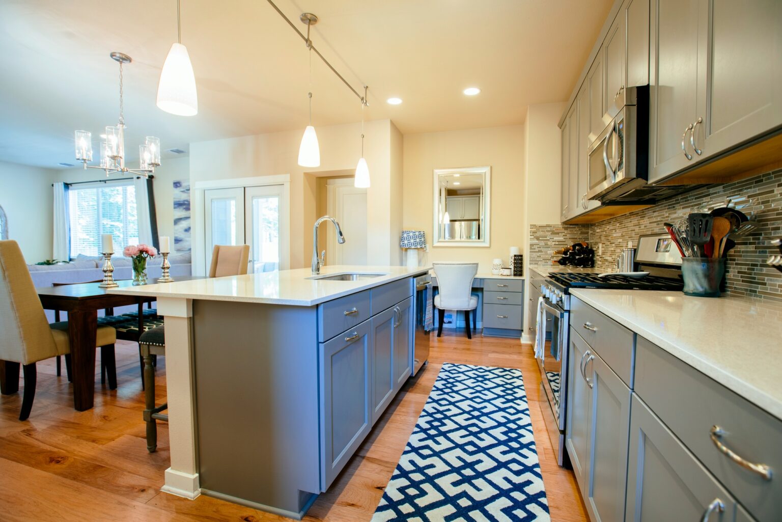 Modern home kitchen diner with green grey fitted units, a kitchen island and blue floor rug.