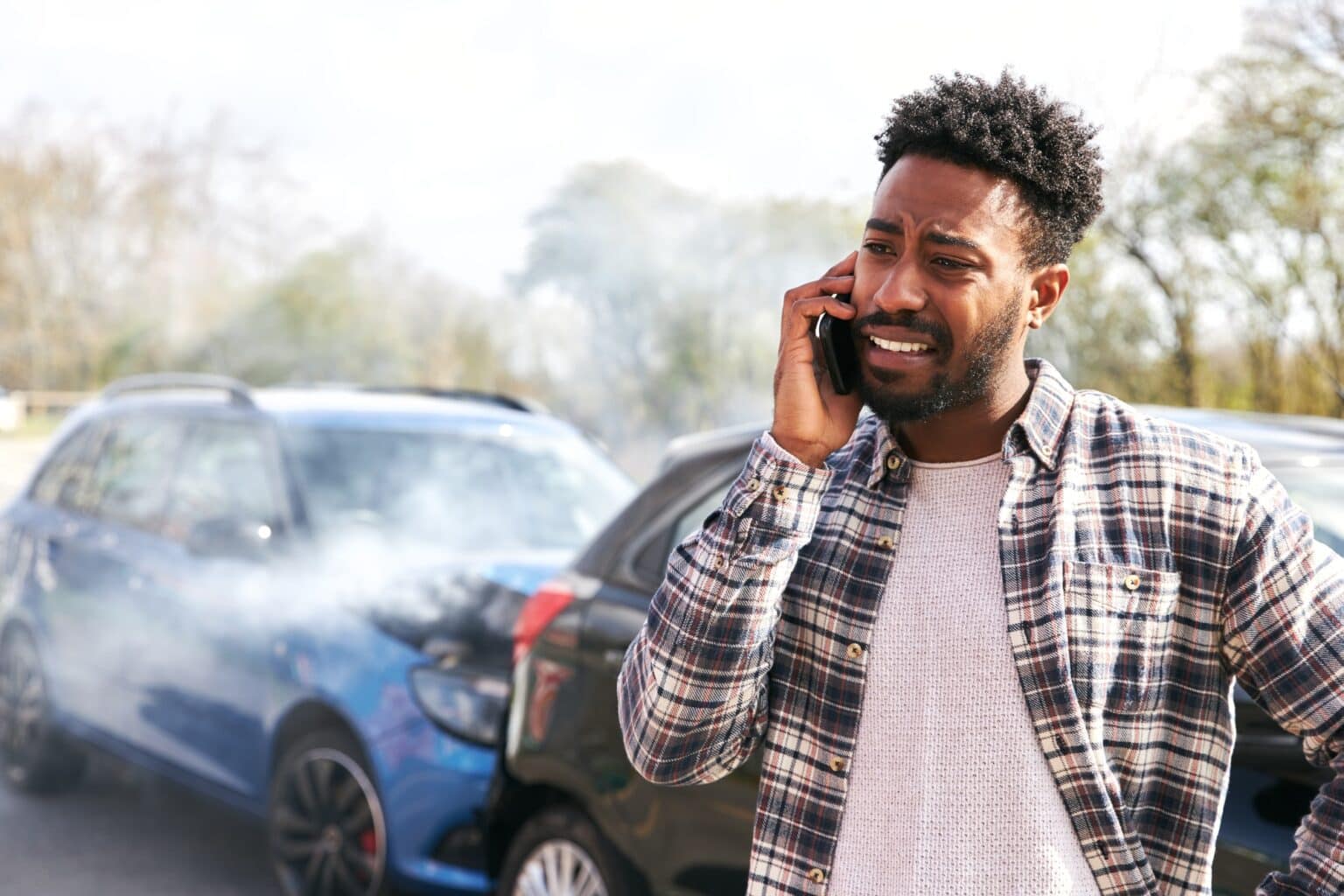 Young Male Driver Calling Car Insurance Company On Mobile Phone After Road Traffic Accident